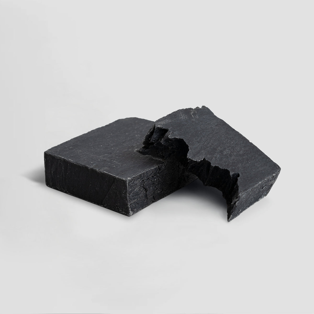 Two pieces of black soap on a light gray background