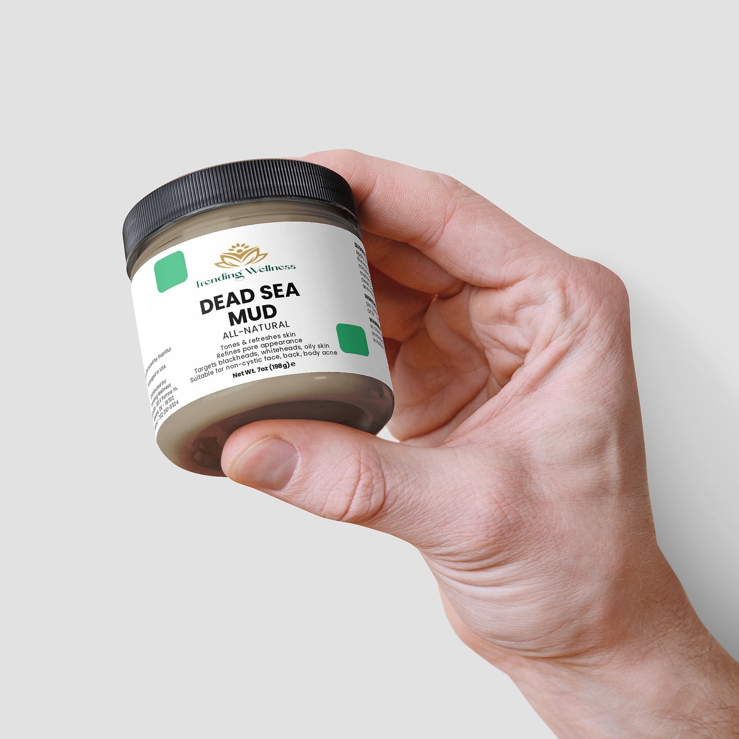 Hand holding a jar of Dead Sea Mud against a light gray background