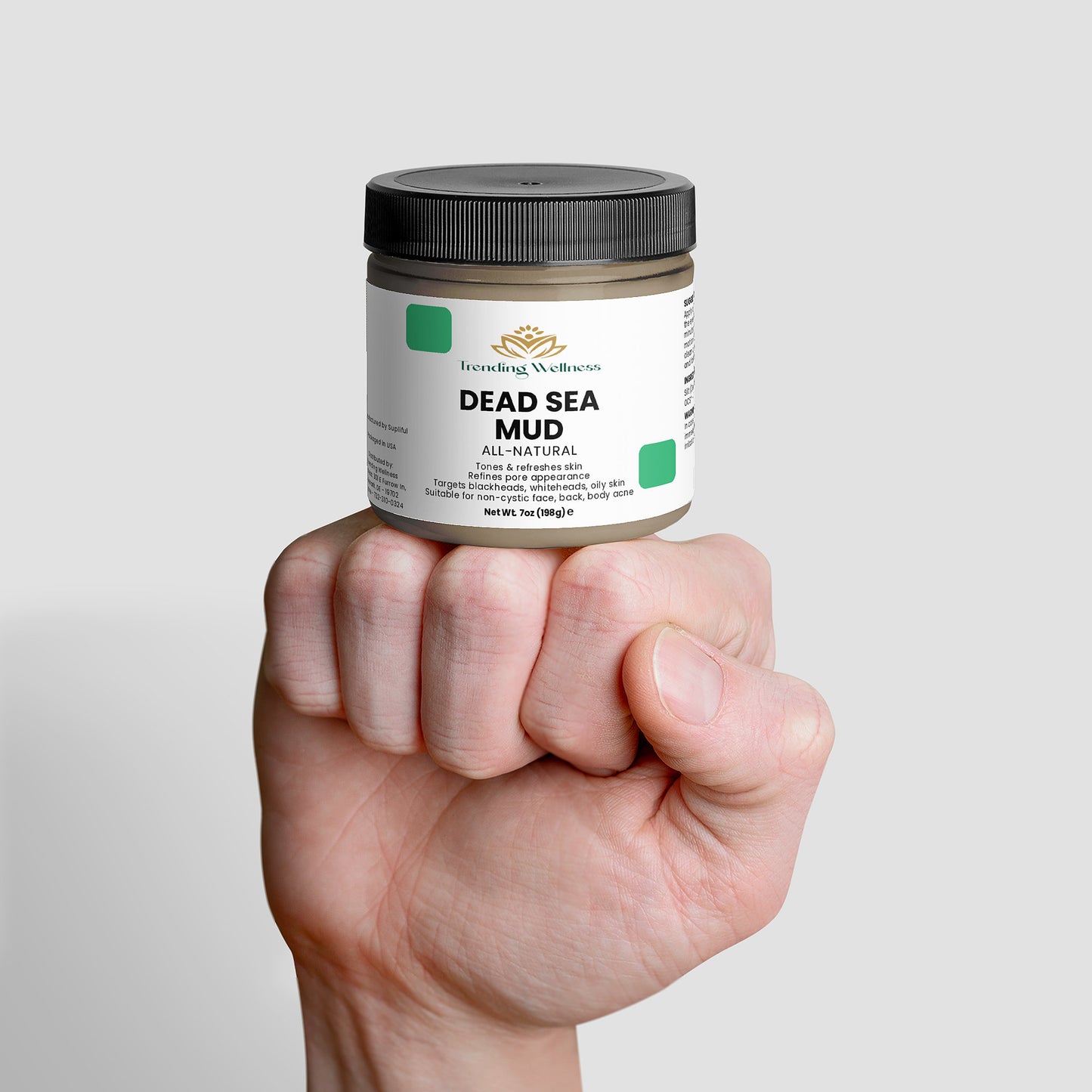 Hand holding a jar of Dead Sea Mud on a light gray background